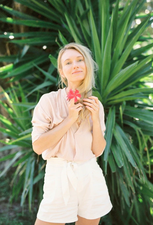 a woman standing in front of a palm tree, a portrait, by Maggie Hamilton, trending on unsplash, holding a flower, sydney sweeney, wearing a linen shirt, hibiscus