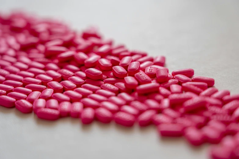 a pile of pink pills sitting on top of a table, by Emma Andijewska, plasticien, up-close, reds, made with millions of stroke, hdpe