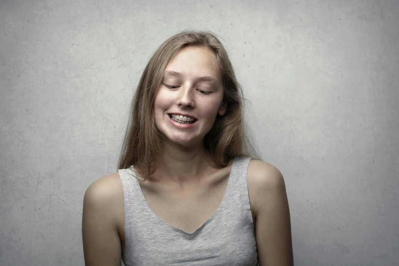 a woman is smiling with her eyes closed, grey backdrop, crooked teeth, teenager, in front of white back drop