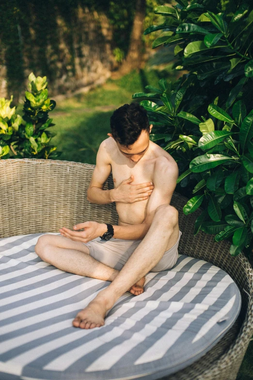 a man sitting on top of a round table, an album cover, by Adam Dario Keel, unsplash, bare chest, in the garden, palm body, heart emblem on chest