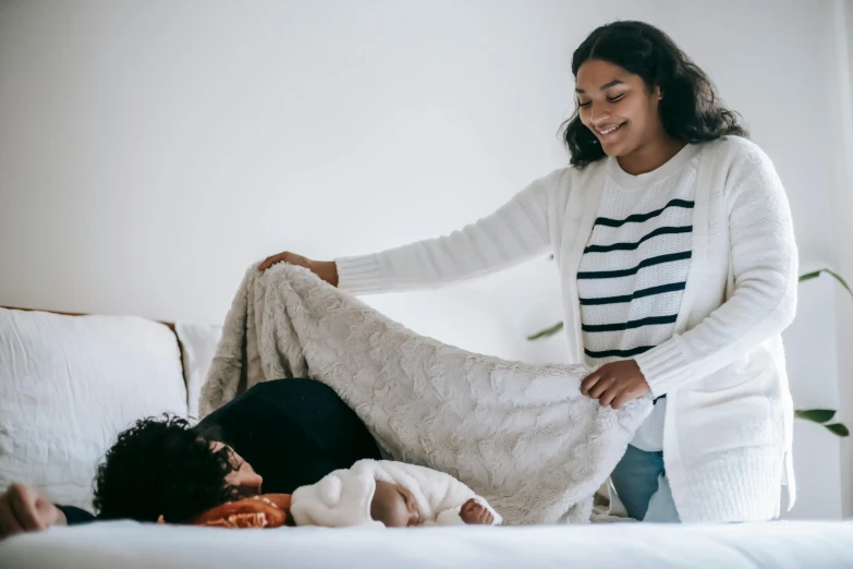 a woman laying on top of a bed next to a baby, pexels contest winner, happening, covered with blanket, manuka, reaching out to each other, diverse