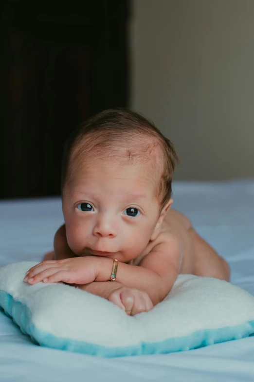 a baby laying on a pillow on a bed, unsplash, happening, cleft chin, blue-eyed, proud looking, tiny mouth