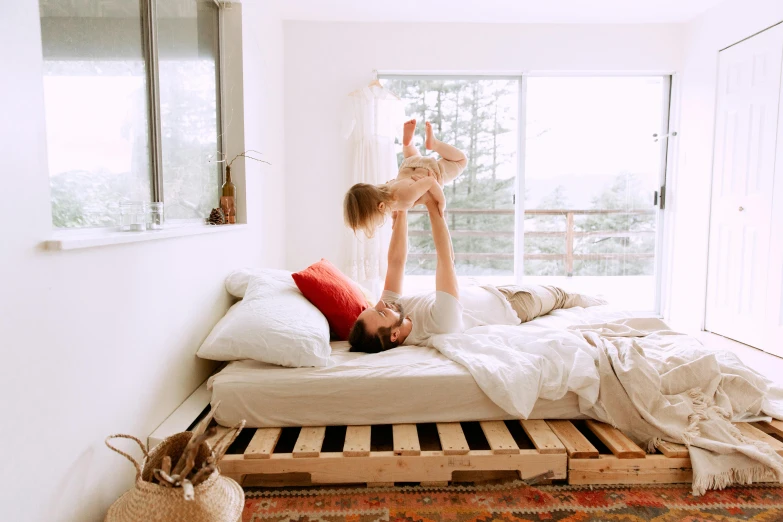 a woman laying on top of a bed next to a window, by Julia Pishtar, pexels contest winner, father with child, pallet, white background, fully functional