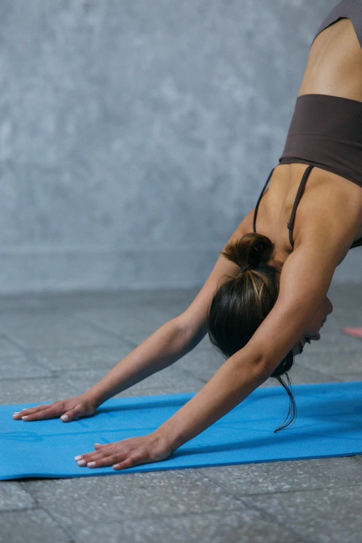 a woman doing a yoga pose on a blue mat, a picture, by Rachel Reckitt, shutterstock, back arched, brown, no cropping, sports clothing