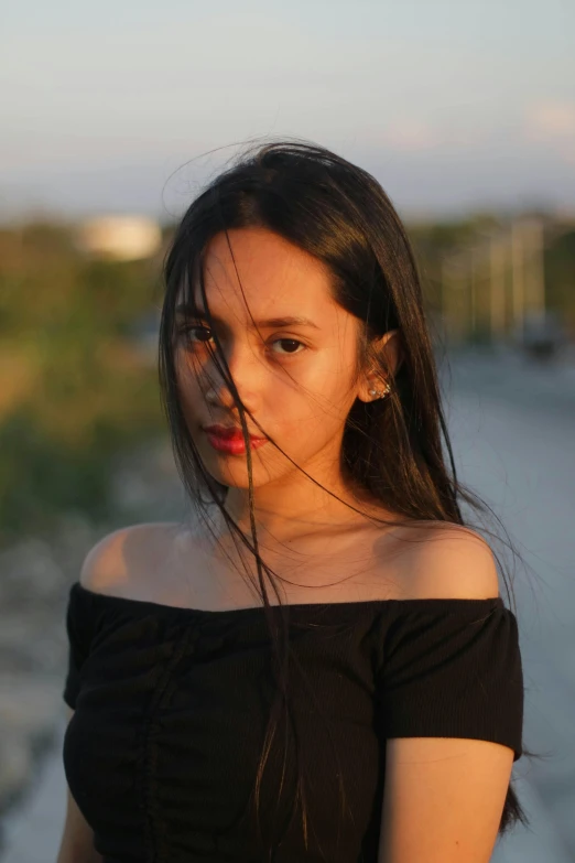 a woman in a black dress standing on a beach, by Robbie Trevino, unsplash, realism, portrait of modern darna, 🤤 girl portrait, straight neck, late evening