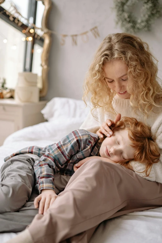 a woman laying on top of a bed next to a child, pexels contest winner, hugging her knees, thumbnail, little boy, soothing