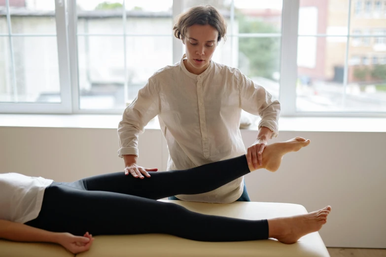 a woman is doing a leg massage in front of a window, by Nina Hamnett, lachlan bailey, on a white table, nimble, highly technical