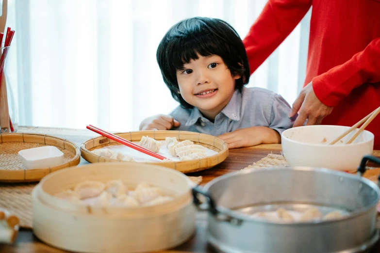 a little boy that is sitting at a table, by Tan Ting-pho, pexels contest winner, dumplings on a plate, tyler edlin and natasha tan, welcoming grin, bowl filled with food