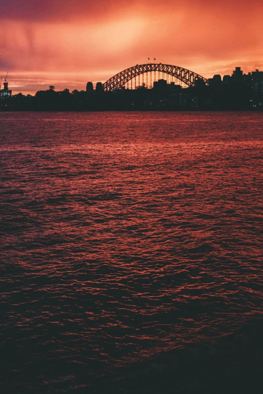 a large body of water with a bridge in the background, inspired by Sydney Carline, pexels contest winner, blood red colored sky, syd, telephoto shot, film photo