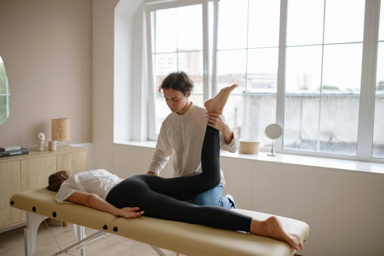 a man sitting on top of a table next to a woman, a picture, by Emma Andijewska, trending on pexels, acupuncture treatment, stretching to walls, leg and hip shot, back and standing