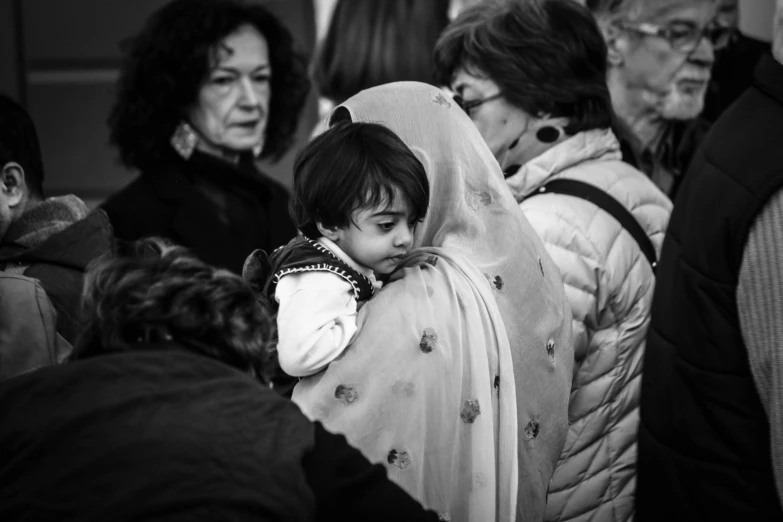 a group of people standing next to each other, a black and white photo, by Giuseppe Avanzi, pexels, qajar art, tiny girl looking on, comforting and familiar, people enjoying the show, wrapped in a black scarf