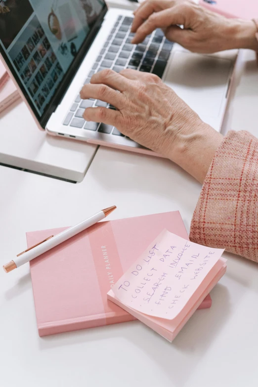 a woman sitting at a desk using a laptop computer, a picture, by Carey Morris, trending on pexels, light pink tonalities, with some hand written letters, an elderly, holding books