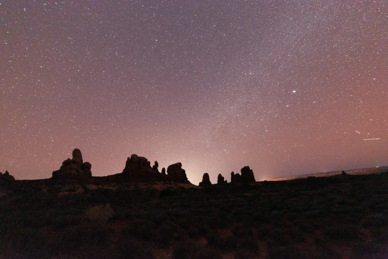 a group of people standing on top of a hill under a sky full of stars, unsplash contest winner, tonalism, tall arches, red sandstone natural sculptures, pink arches, tall stone spires