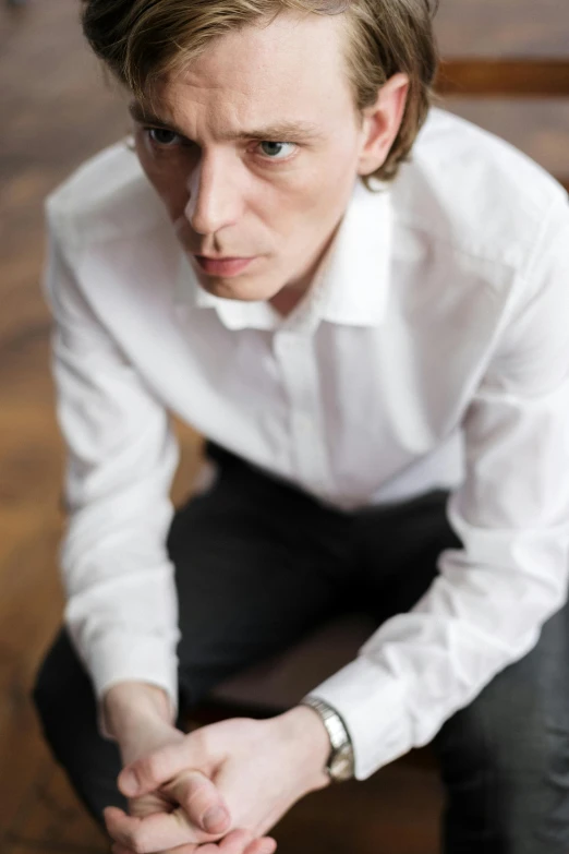 a man in a white shirt and black pants, an album cover, inspired by Alexander Kanoldt, headshot photograph, david bates, photographed for reuters, looking away from camera