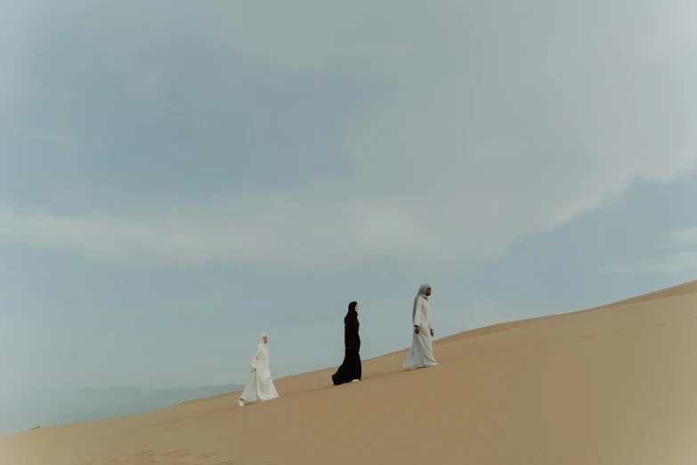 a group of people standing on top of a sandy beach, by Ahmed Yacoubi, unsplash contest winner, surrealism, three women, wearing simple robes, walk in a funeral procession, ( ( theatrical ) )