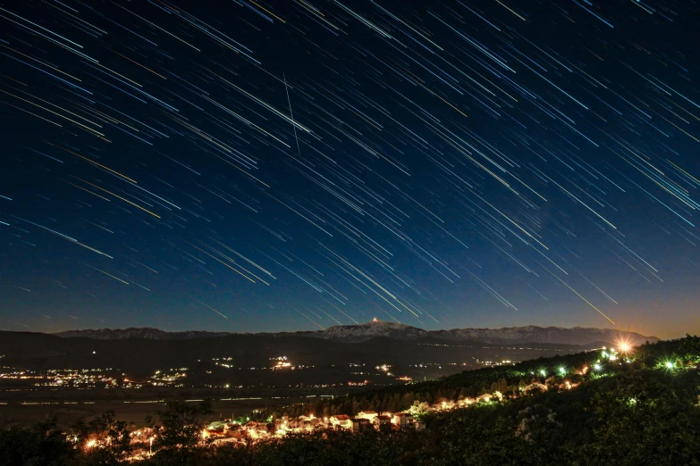 star trails streak across the night sky over a town, unsplash contest winner, renaissance, distant mountains lights photo, asteroid belt in distance, instagram photo, falling star on the background