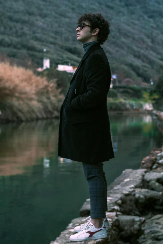 a man standing on a rock next to a body of water, black overcoat, male ulzzang, shot with sony alpha, thoughtful )