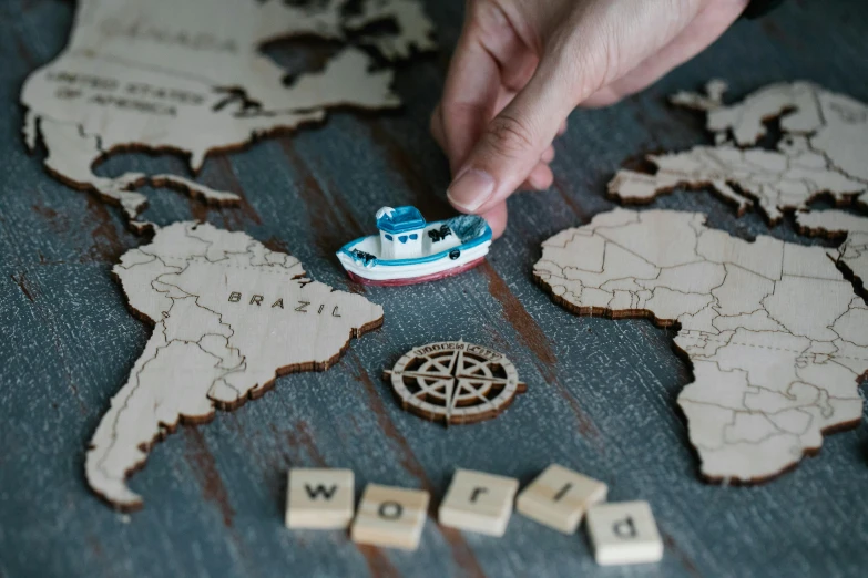 a person placing a toy boat on top of a map, a jigsaw puzzle, by Julia Pishtar, engraved, wooden boat, all these worlds are yours, medium close up shot