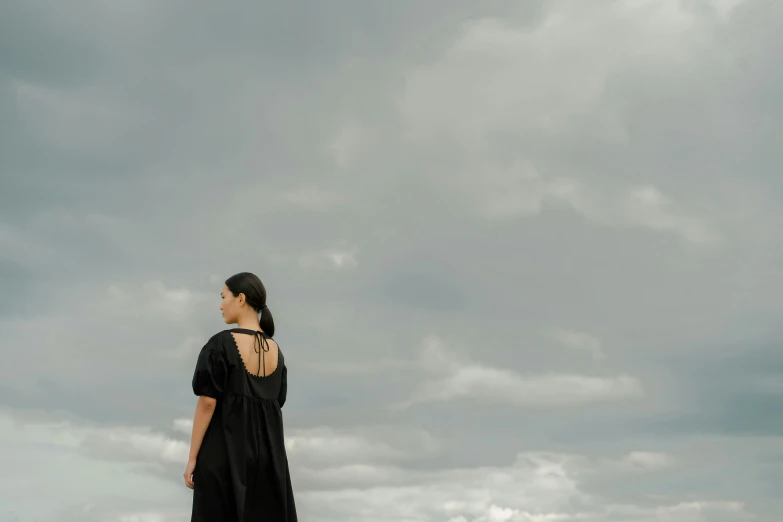 a woman standing on top of a lush green field, a portrait, pexels contest winner, conceptual art, the sky is black, gray sky, wearing a black dress, standing on rooftop