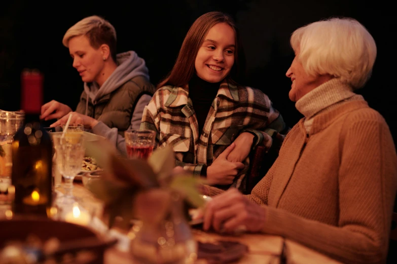 a group of people sitting at a dinner table, in the evening, warm features, family friendly, female looking