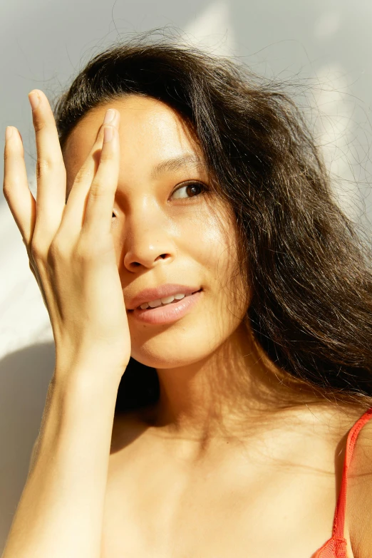 a woman in a red bikini posing for a picture, an album cover, trending on pexels, hands shielding face, detailed face of a asian girl, diffuse natural sun lights, skincare