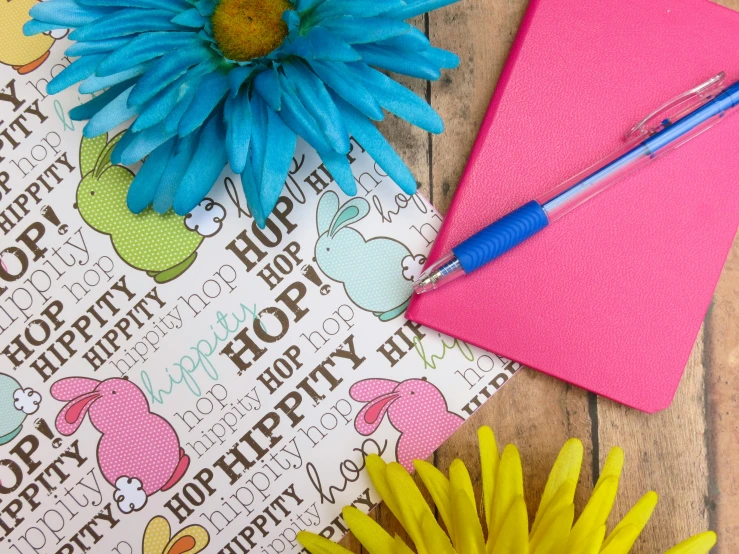 a blue pen sitting on top of a pink notebook next to a flower, inspired by Peter Alexander Hay, graffiti, a rabbit full of hope, handcrafted paper background, spring theme, happy colours