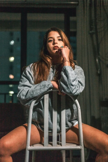 a woman sitting on a chair smoking a cigarette, inspired by Elsa Bleda, trending on unsplash, bra and shorts streetwear, gray hoodie, young teen, doing a sassy pose