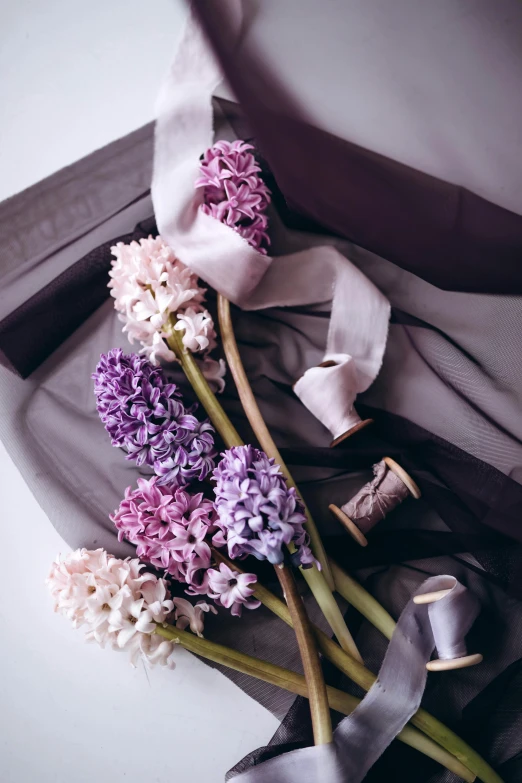 a bunch of flowers sitting on top of a table, inspired by Pierre-Joseph Redouté, trending on unsplash, romanticism, purple cloth, hyacinth, ribbons, earthy light pastel colours