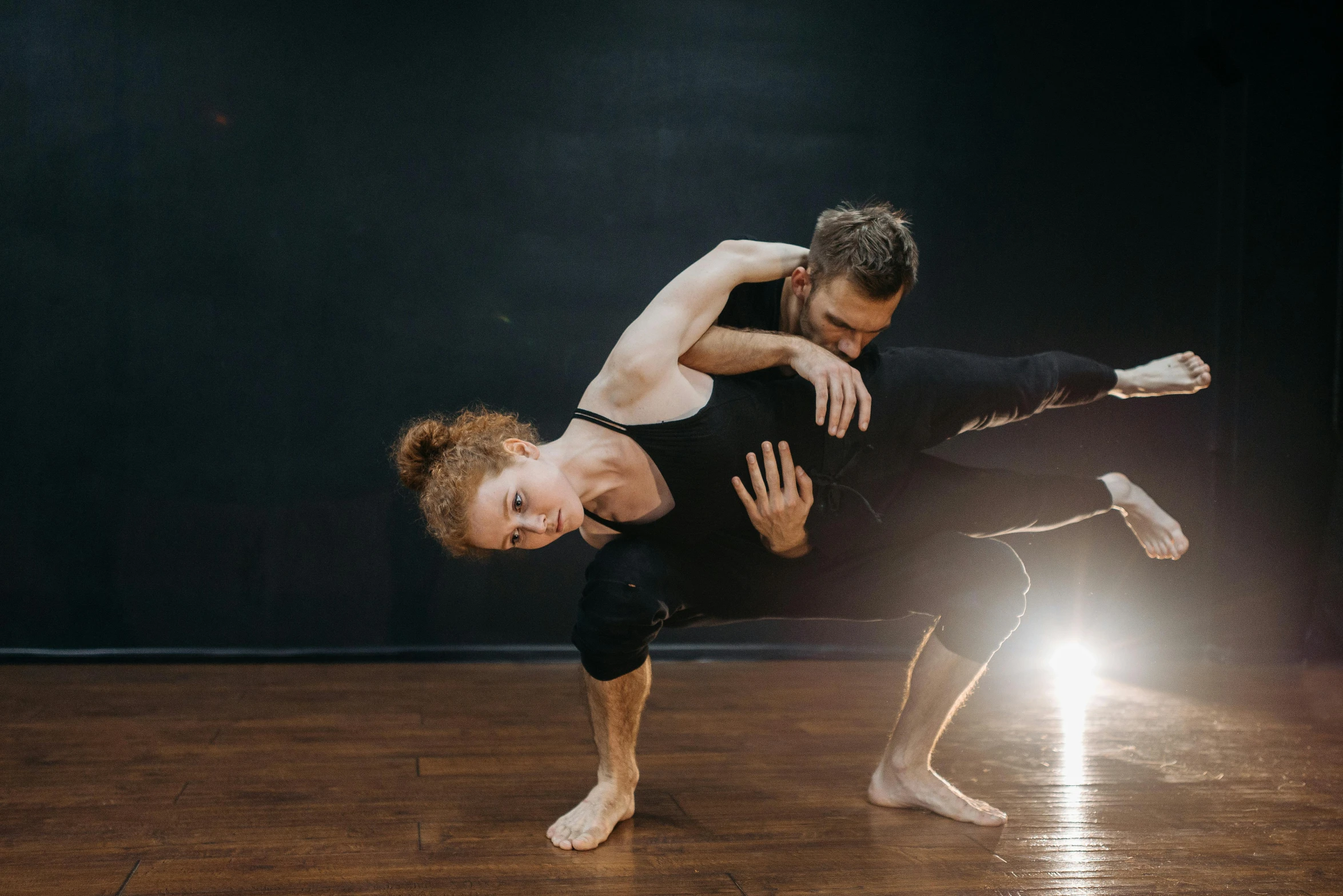 a man and woman doing a handstand on a wooden floor, a portrait, by Jessie Algie, unsplash, arabesque, sydney hanson, woman holding another woman, spiraling, illuminated