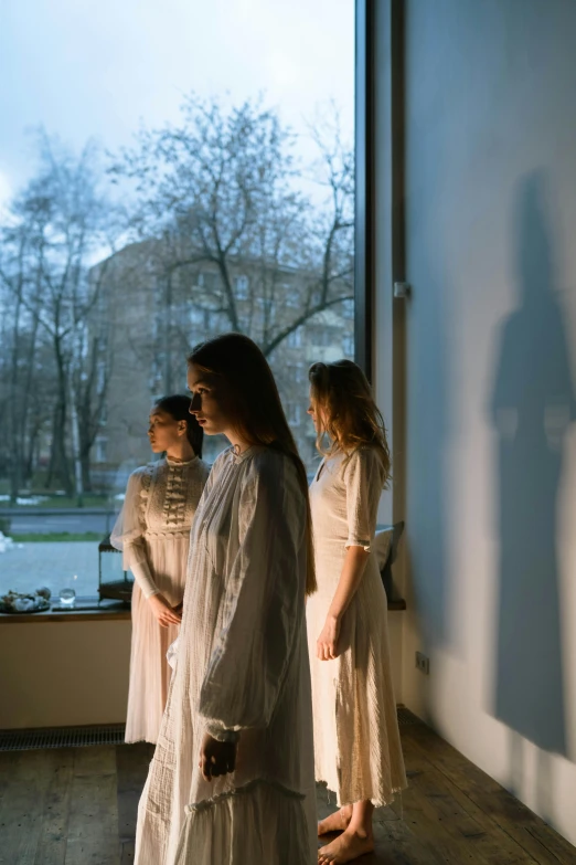 a group of people standing in front of a window, inspired by Anna Füssli, romanticism, 3 sisters look into the mirror, dawn lighting, cast shadows, spring evening