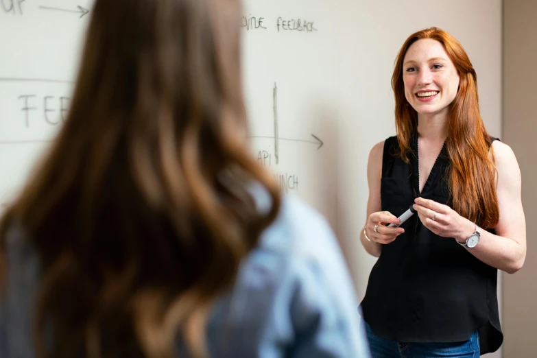 a woman standing in front of a whiteboard with writing on it, pexels contest winner, academic art, smiling at each other, hr ginger, shallow depth, lachlan bailey