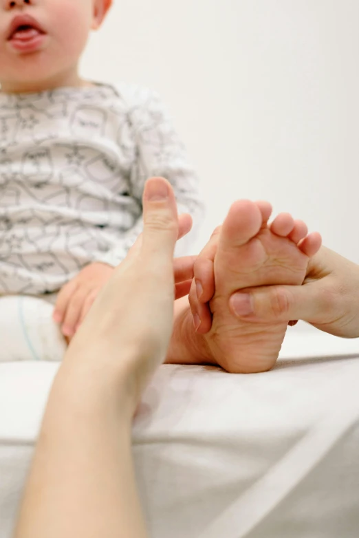 a baby sitting on top of a bed next to a woman, unsplash, mingei, focus on his foot, medical image, square, for kids