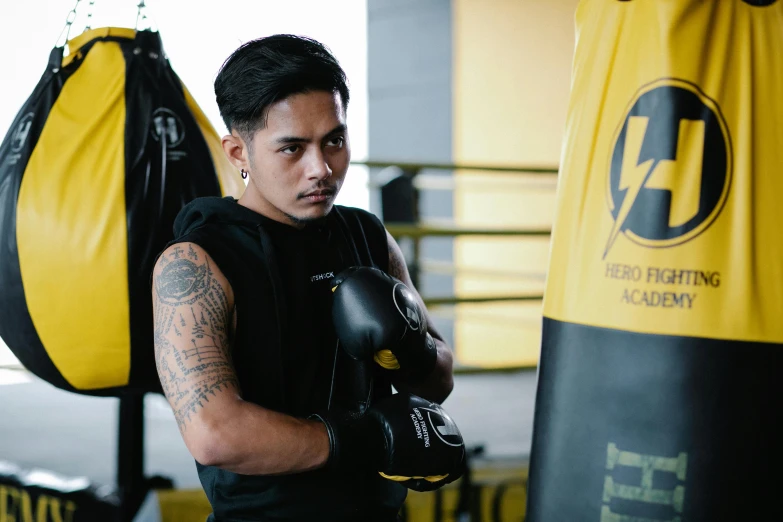 a man standing next to a punching bag, inspired by Eddie Mendoza, pexels contest winner, yellow and black color scheme, ngai victo and dougherty patrick, tattooed, hidari and vlop