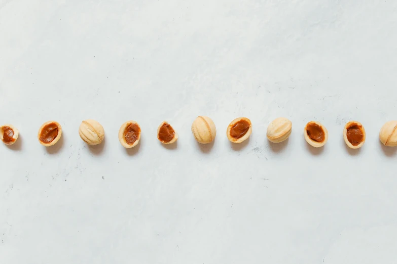 nuts arranged in a row on a white surface, an album cover, inspired by Károly Patkó, trending on pexels, hurufiyya, pale orange colors, 6 pack, rounded shapes, ochre