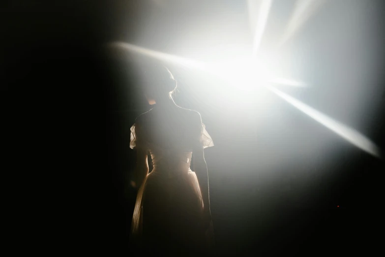 a woman standing in front of a bright light, by Adam Chmielowski, searchlight, show, woman in dress, under a spotlight