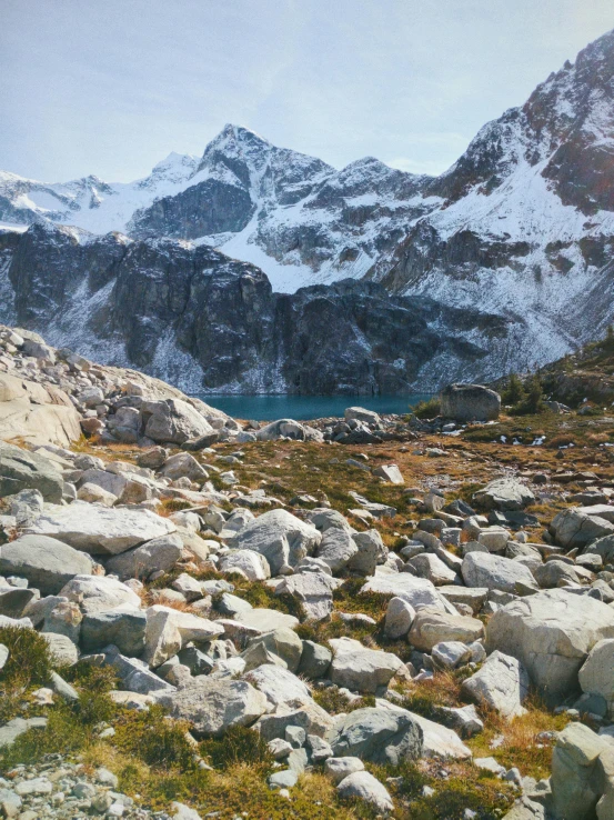 a man standing on top of a rocky hill next to a lake, an album cover, unsplash contest winner, photorealism, snowy craggy sharp mountains, stephen shore, british columbia, slide show