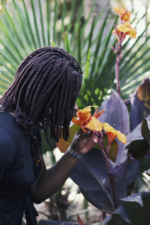 a woman with dreadlocks looking at a flower, inspired by Ras Akyem, pexels contest winner, big leaves, exterior botanical garden, bahamas, grey