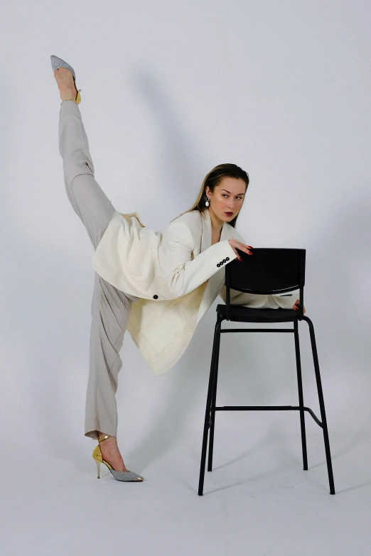 a woman sitting on a chair in front of a laptop, by Carey Morris, trending on pexels, arabesque, high kick, white suit, macho pose, dressed with long fluent clothes