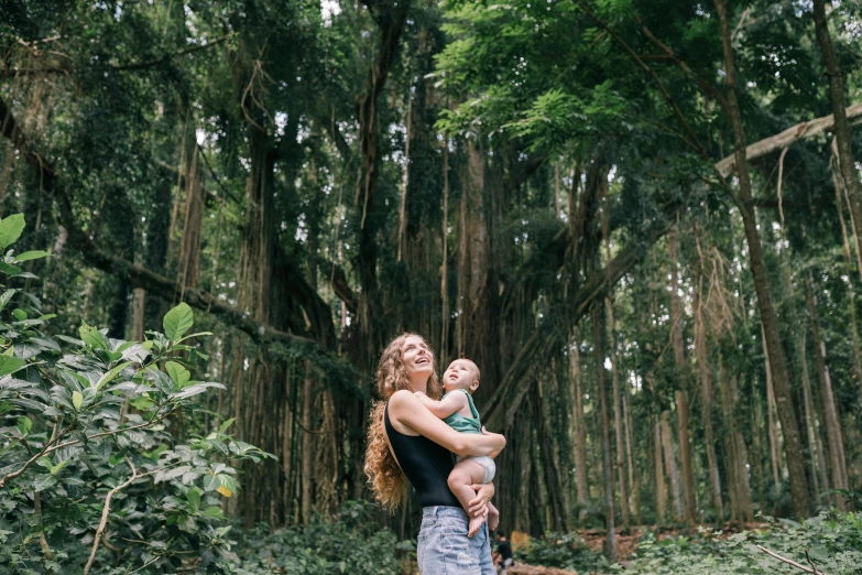 a woman holding a baby in a forest, pexels contest winner, happening, kauai, avatar image, exotic trees, exterior shot