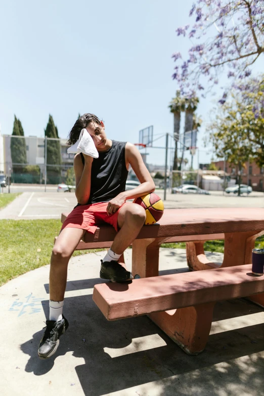 a man sitting on a bench with a basketball ball, heat wave, hungover, boy shorts, on a table