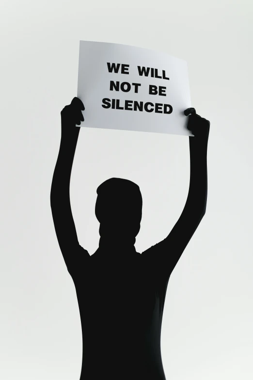 a man holding a sign that says we will not be silenced, a poster, inspired by Vanessa Beecroft, shutterstock, silhouette, solitude, 2 0 0 0 s, noise