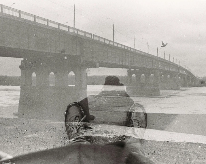 a black and white photo of a person sitting in front of a bridge, inspired by Vivian Maier, surrealism, multiexposure, rainy; 90's photograph, cars and people, clear reflection