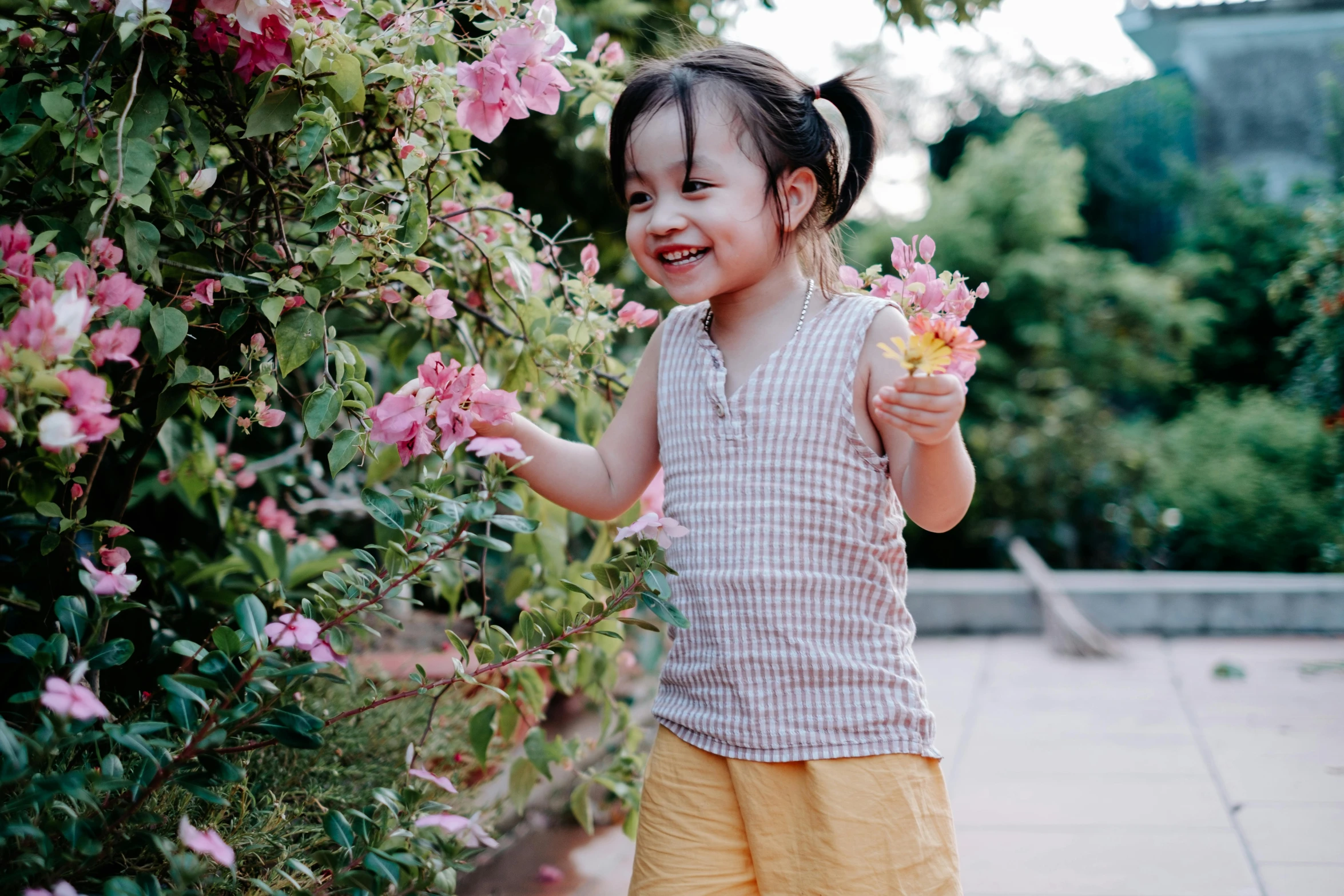a little girl standing next to a bush of flowers, inspired by Cui Bai, pexels contest winner, smiling playfully, sleeveless, asian female, dressed in a top and shorts