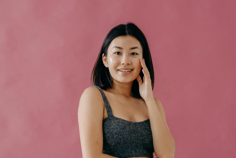 a woman talking on a cell phone in front of a pink wall, a character portrait, inspired by Ruth Jên, trending on pexels, happening, asian beautiful face, wearing a cropped black tank top, skin care, on grey background