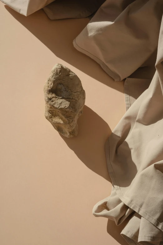 a rock sitting on top of a table next to a pair of pants, unsplash contest winner, visual art, sand color, desert robe, ignant, high angle close up shot