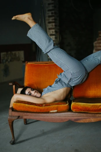 a woman laying on top of an orange couch, inspired by Balthus, pexels contest winner, arabesque, wearing pants, male model, gif, contorted