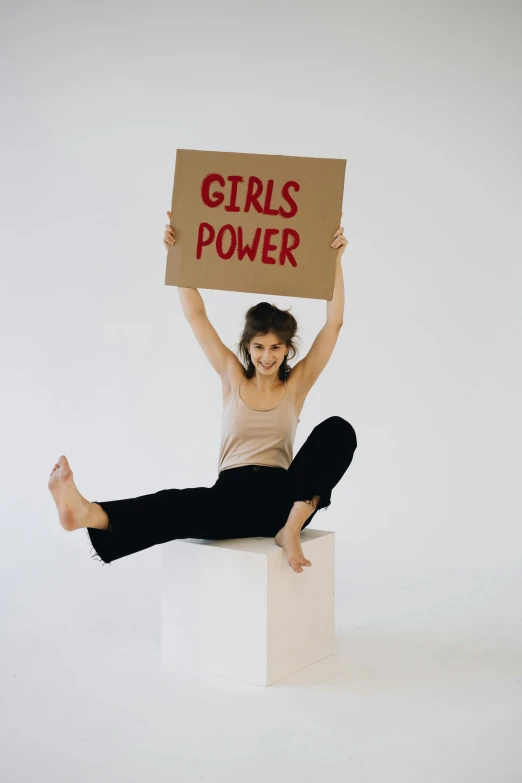 a woman holding a sign that says girls power, an album cover, trending on pexels, hero pose, girl with brown hair, grey, i_5589.jpeg
