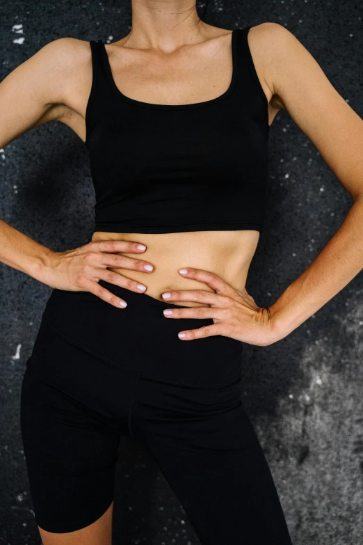 a woman standing with her hands on her hips, trending on pexels, wearing a cropped black tank top, heavy gesture style closeup, detailed product image, contorted