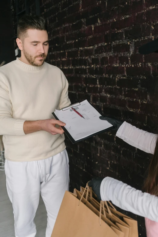 a man standing next to a woman holding shopping bags, by Adam Marczyński, pexels contest winner, renaissance, signing a bill, wearing a white sweater, gif, wearing polo shirt