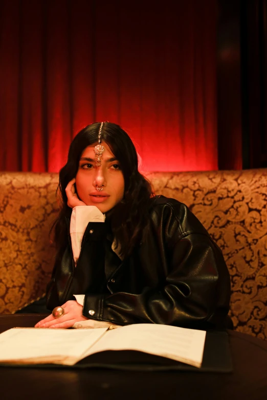 a woman sitting on a couch reading a book, an album cover, reddit, with his long black hair, wearing leather coat, transgender, sitting on a mocha-colored table